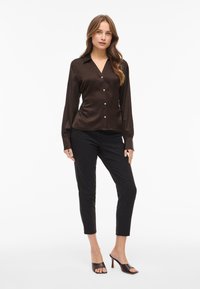 Brown satin button-up shirt with a collar, long sleeves, and a fitted design, paired with black tailored pants and open-toe heels.