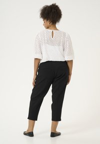 Haut blanc avec un motif découpé hexagonal, manches courtes et un détail en forme de trou de serrure au dos ; associé à un pantalon cropped noir et des ballerines.