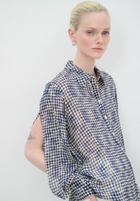 Camicia trasparente con bottoni caratterizzata da un motivo a pois in blu navy e crema. Vestibilità rilassata con maniche corte e larghe e colletto.