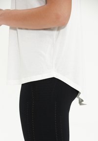 Vit kortärmstopp med en böjd nederkant, tillsammans med svarta strukturerade leggings med vertikala ränder och subtila utskärningar.