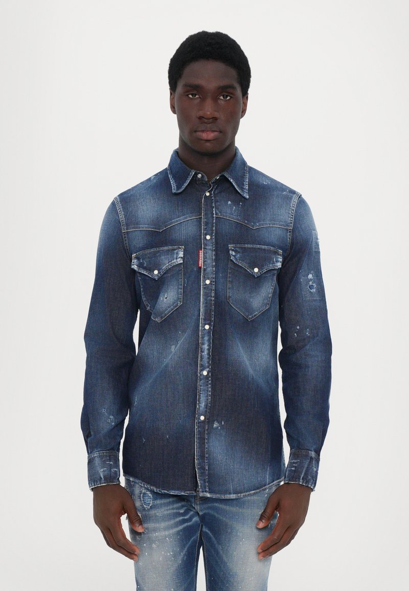 Denim shirt with a dark blue wash, pointed collar, front pockets, and distressed details. Long sleeves with button cuffs.