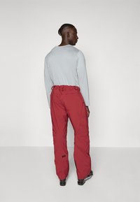 Pantalons imperméables rouges avec ceinture élastique, design à jambe droite et accents de logo. Texture lisse et matériau durable adapté pour une utilisation en extérieur.