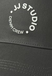 Black cap with a textured fabric, featuring raised white lettering: "JJ STUDIO" in a circular design and "DENIM CREW" underneath.