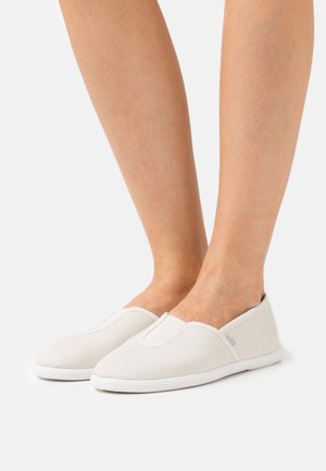 Sapatilhas brancas de lona, tipo slip-on, com bico arredondado, inserções elásticas nas laterais e sola de borracha branca texturizada. Design simples e minimalista.