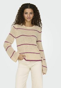 Crèmekleurige trui met paarse horizontale strepen, met een gestructureerde brei, brede mouwen en een ronde halslijn, gecombineerd met lichte broek.
