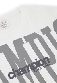 Bílý bavlněný tričko s velkým šedým textem "champion" a "NEW YORK", s kulatým výstřihem a měkkou texturou.