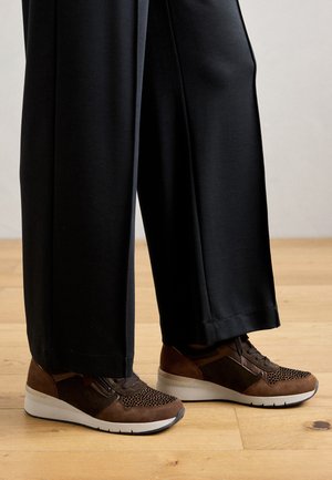 Brune sneakers med en blanding av semsket skinn og mesh-materialer, med en teksturert overdel, hvit såle og kontrasterende detaljer. Kombinert med svarte bukser.