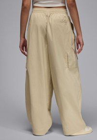 Beżowe spodnie cargo z szerokimi nogawkami, elastycznym paskiem w talii, bocznymi kieszeniami i gładkiego, lekkiego materiału; cięte w luźnym, swobodnym kroju.