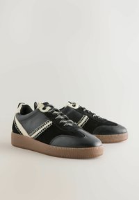Schwarze und beige Sneakers aus einer Kombination von Leder und Wildleder, mit einer strukturierten Gummisohle und gemusterten Schnürsenkeln für zusätzliche Details.
