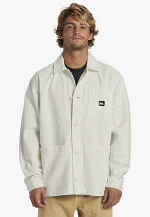 Lightweight cream jacket with a collared neck, button closure, and front pockets. Features a small black logo on the left chest pocket.