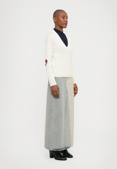 Cream v-neck sweater with textured knit and heart logo on the sleeve, paired with a high-waisted denim skirt in light gray and blue. Black heeled boots.
