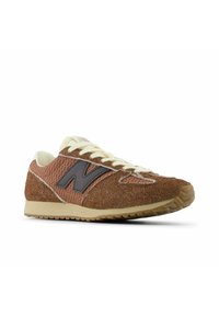 Brown and beige New Balance sneaker with suede and mesh materials, cream laces, and a black "N" logo on the side, angled left on a white background.