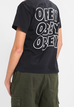 T-shirt in cotone nero con grande scritta bianca "OBEY" stampata sul retro. Taglio comodo, con maniche corte e design a girocollo.