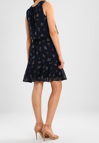 Navyblaues Blumenkleid mit ärmellosem Design, fließendem Rock und Bindeband auf der Rückseite. Es zeichnet sich durch eine durchsichtige Textur und zarte Blumenmuster aus.