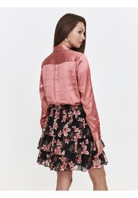 Różowa satynowa bluzka z długimi rękawami, w zestawieniu z czarną spódnicą z falbanami w kwiaty z różowymi i zielonymi akcentami.