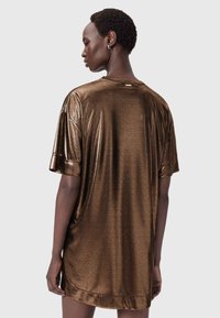 Brun metallisk oversized t-shirt med korta ärmar, mjuk struktur och rundad halsringning. Har en subtil detalj på baksidan med sömmar.