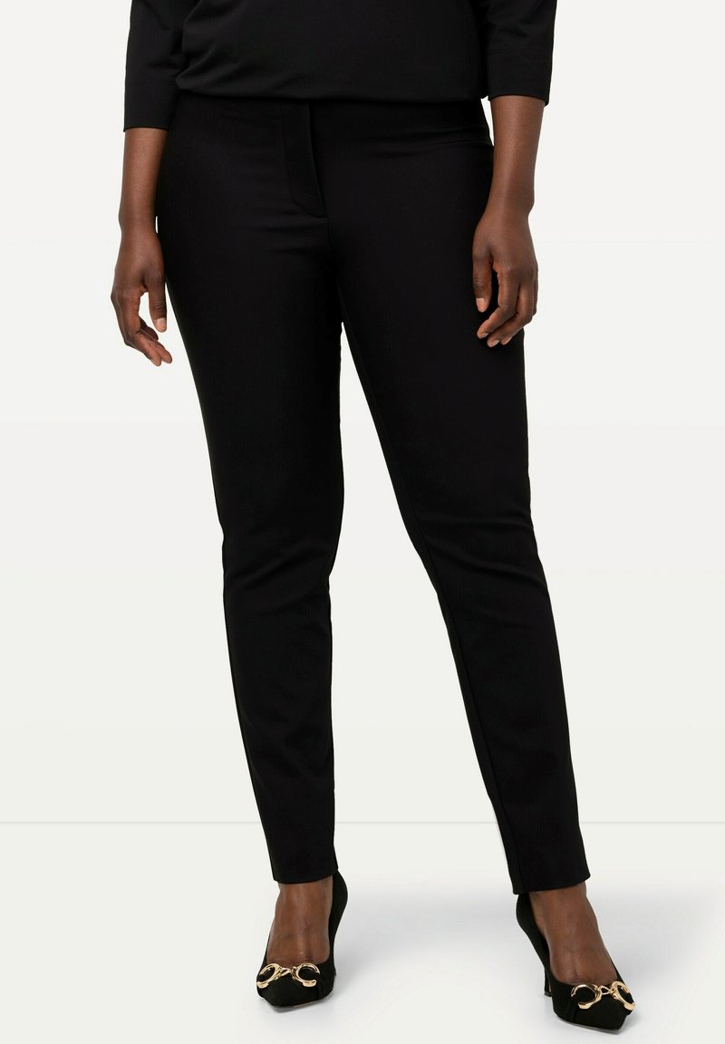 Czarne dopasowane spodnie o gładkiej fakturze, średnim stanie i zwężających się nogawkach. Połączone z czarnymi butami z złotymi akcentami.