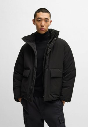 Black padded jacket with a high collar, zip closure, and two front pockets. Features a smooth texture and a loose fit design.