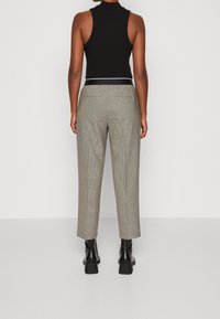 Musta ribbattu hihaton toppi yhdistettynä vaaleanharmaisiin ruudullisiin housuihin, joissa on rento istuvuus ja kaksi takataskua, täydentäen asua mustilla lohkopohjakorollisilla saappailla.