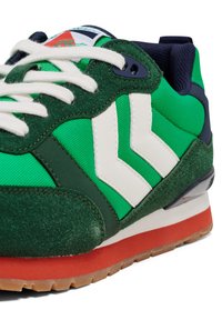 Grønn og marineblå sneaker med hvite detaljer. Har en blanding av teksturert semsket skinn og mesh-materialer. Gummisåle med oransje detaljer og tykke lisser.