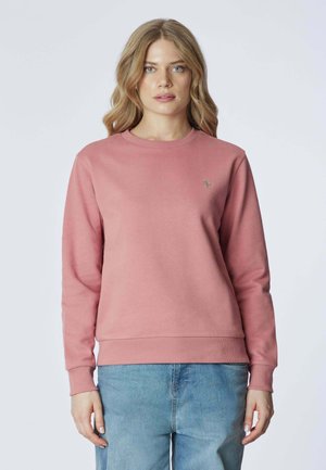 Felpa rosa con maniche lunghe, polsini e orlo a coste, collo a giro, con un piccolo ricamo sul lato sinistro del petto. Abbinata a jeans blu chiaro.