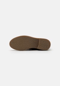 Suela negra de zapato con un patrón de goma texturizada y entresuela marrón. Punta redondeada y tacón ligeramente elevado. Diseño limpio y plano sin adornos.