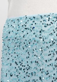 Helle blaue Stoff mit schimmernden Pailletten in unterschiedlichen Farbtönen, die eine strukturierte, gemusterte Oberfläche schaffen.