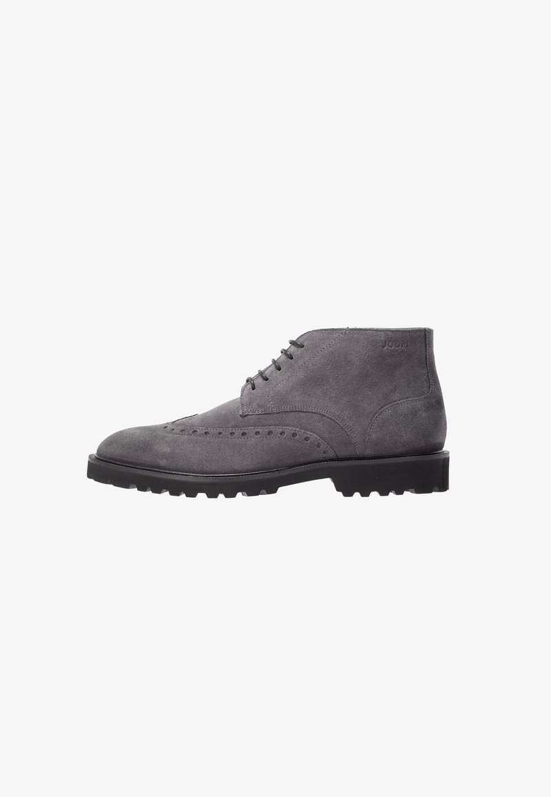 Bottine homme en daim gris avec détails brogue, semelle à crampons noire et fermeture à lacets, inclinée pour montrer le côté extérieur.