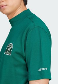 Green cotton t-shirt with a high neck. Features embroidered "adidas originals" logo on the chest and a small white logo on the sleeve.