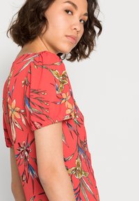 Vestido floral vermelho com mangas curtas em balão, com padrões florais detalhados em amarelo, laranja e verde, feito de tecido leve.