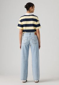 Ριγέ μπλε και κίτρινο κοντομάνικο πόλο πουκάμισο συνδυασμένο με ανοιχτό μπλε τζιν παντελόνι με φαρδιά μπατζάκια, διακοσμημένο με ταμπέλα λογότυπου στο πίσω μέρος και ξεθωριασμένη υφή.