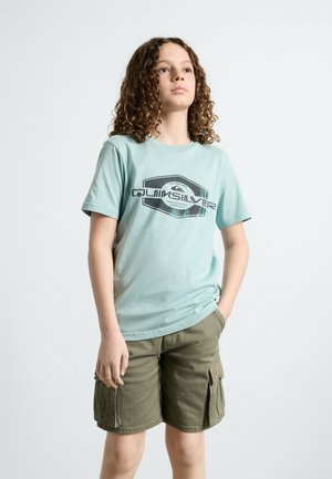 Lichtblauw t-shirt met een zwart grafisch ontwerp en logo, gecombineerd met olijfgroene cargoshorts met zijzakken.