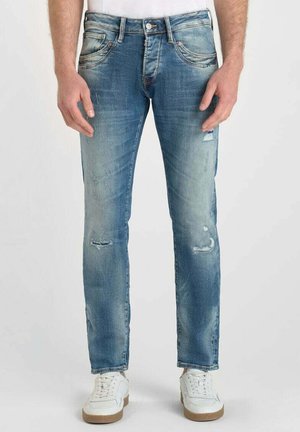 Jean en denim bleu clair avec une coupe slim, présentant des effets de déchirure et de décoloration. Design standard à cinq poches et braguette à boutons.