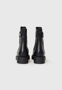Bottines en cuir noir avec une finition légèrement brillante. Équipées d'une accent de boucle, de panneaux élastiques sur les côtés et d'une semelle en caoutchouc épaisse.