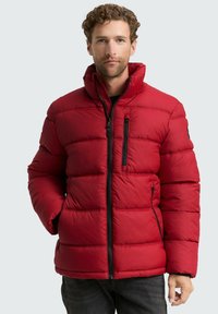 Crvena puf jakna s horizontalnim šavovima, visokim ovratnikom i zatvorenim džepovima s crnim hardverom. Materijal izgleda glatko i izolirano.