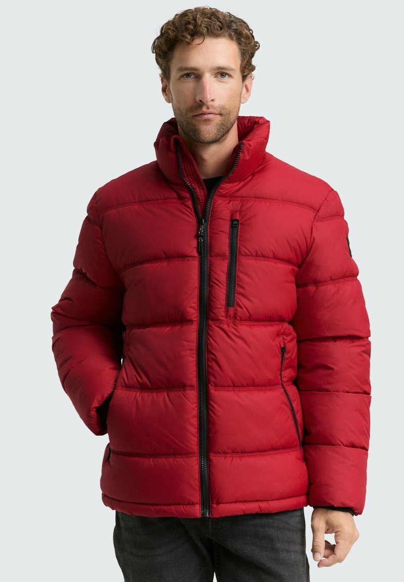 Crvena puf jakna s horizontalnim šavovima, visokim ovratnikom i zatvorenim džepovima s crnim hardverom. Materijal izgleda glatko i izolirano.