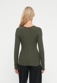 Olijfgroene ribbed top met lange mouwen en een aansluitende pasvorm, ronde halslijn en subtiele naaddetails, gecombineerd met donkere broeken.