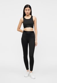 Top corto deportivo negro y leggings de cintura alta a juego, ambos hechos de un material liso y elástico, combinados con zapatillas deportivas blancas.