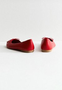 Ballerine in pelle rossa con una texture liscia, punta arrotondata, suola sottile e un fiocco decorativo sulla parte anteriore.