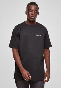 Sort bomulds T-shirt med korte ærmer, der har teksten "glemte ansigtter" i hvidt på det øverste venstre brystområde.