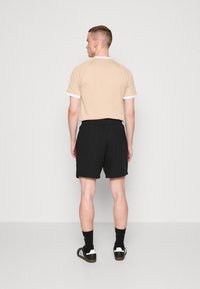 Short-sleeve beige T-shirt with white accents, paired with black shorts. Casual design; smooth texture and relaxed fit.