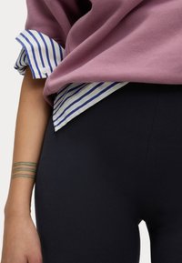 Paarse sweatshirt met opgerolde mouwen over een wit en blauw gestreept shirt, gecombineerd met zwarte legging. Heeft een gladde textuur en een fitted ontwerp.