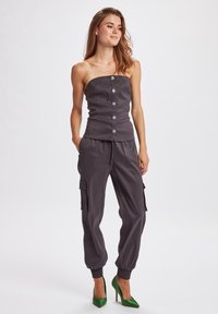 Top grigio senza spalline con bottoni frontali abbinato a pantaloni cargo grigi e scarpe col tacco verde. Il tessuto appare liscio con una finitura opaca.
