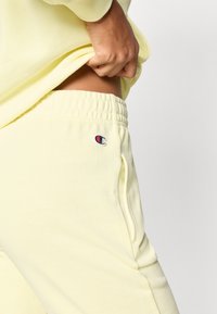 Κίτρινο βαμβακερό παντελόνι jogger με ελαστική μέση, πλαϊνές τσέπες και μικρό κεντ ημένο λογότυπο στον αριστερό μηρό. Μαλακή υφή.