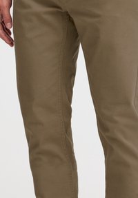 Khaki bavlněné kalhoty mají slim fit střih a hladkou texturu, s kontrastním prošíváním podél bočních švů. Bez viditelného kování nebo vzorů.