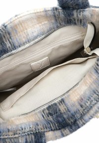 Innenraum einer Woll-Handtasche mit zwei Stofftaschen, heller beiger Fütterung und einem Reißverschlussfach. Der Außenstoff hat ein blau-beiges Muster.