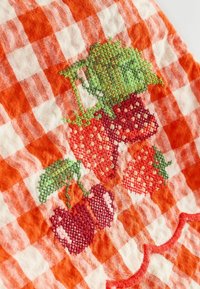 Besticktes kariertes Küchentuch in Orange und Weiß. Zeigt Erdbeeren und Kirschen in rotem und grünem Garn. Strukturierter Stoffdetails.