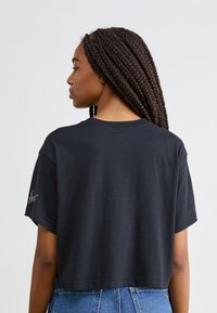 Zwart cropped t-shirt met korte mouwen, gemaakt van zachte katoen. Heeft een ronde halslijn en een klein decoratief logo op de linkermouw.