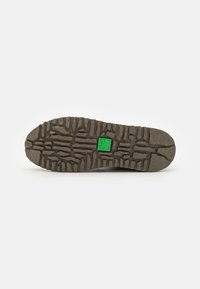 Suela de zapato de goma con un patrón de relieve profundo; color gris con un acento cuadrado verde en el centro. Texturizada para ofrecer tracción y durabilidad.