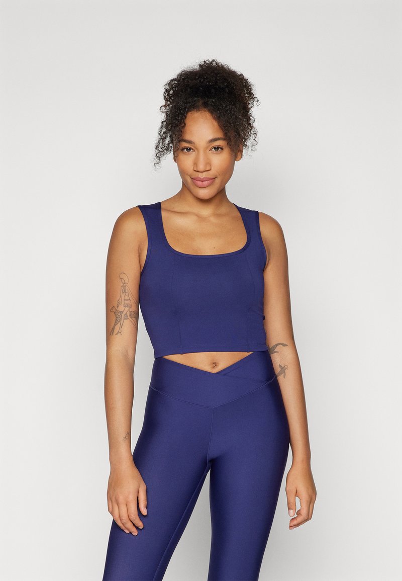Navy plavi crop top s kvadratnim izrezom, uparen s hlačama visokog struka koje imaju križni dizajn. Glatki, rastezljivi materijal.